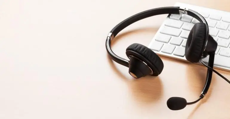Black headset with a microphone resting on a white computer keyboard on a light wooden desk—perfect for storage unit management or coordinating tasks using self storage software.