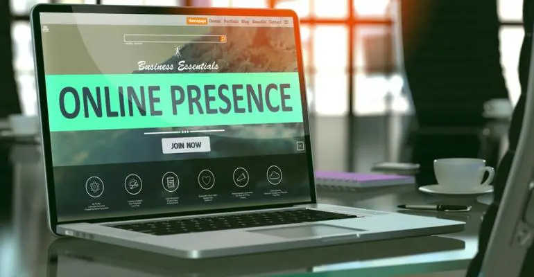 A laptop on a desk displays a website with the text "ONLINE PRESENCE" in large letters, showcasing storage unit management tools, in an office setting with sunlight streaming through the windows.