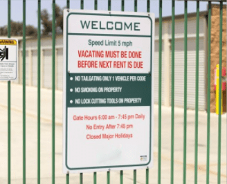 A sign on a gate lists storage facility management rules, including a 5 mph speed limit, no smoking, and gate hours from 6:00 am to 7:45 pm.