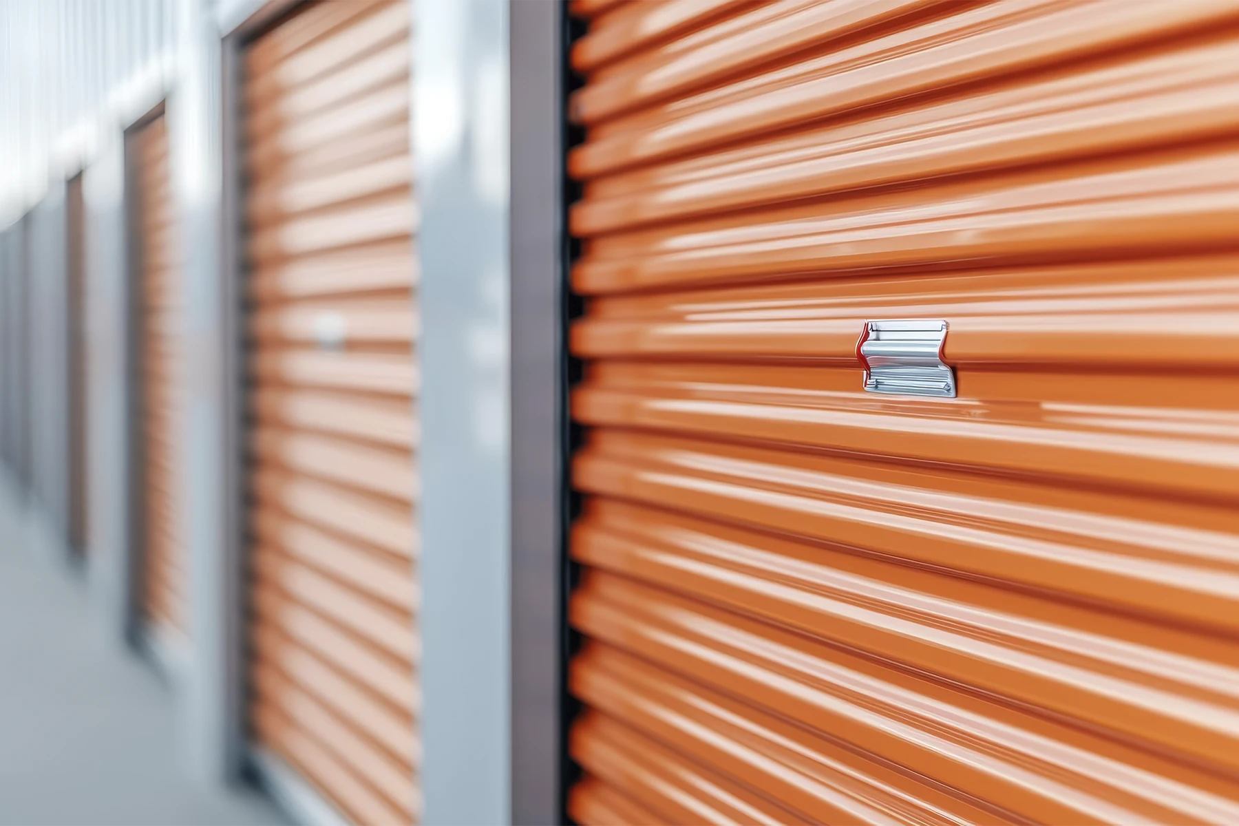 Row of orange roll-up storage unit doors with silver latches in a self-storage facility, shown at an angle—perfect for facilities seeking efficient storage unit management or using self storage software.