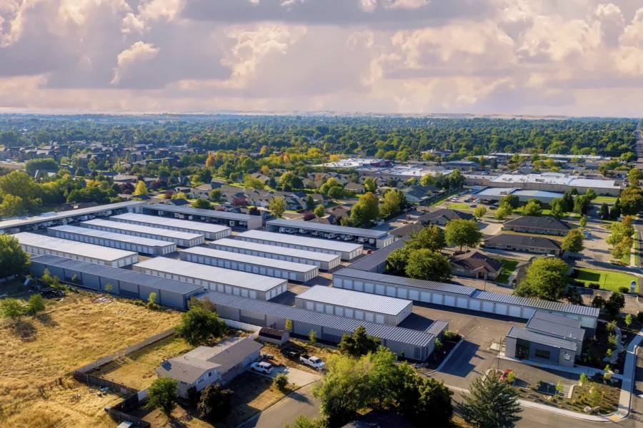 Aerial view of a large self-storage facility, efficiently run with modern self storage software, surrounded by residential houses, green trees, and streets under a partly cloudy sky.
